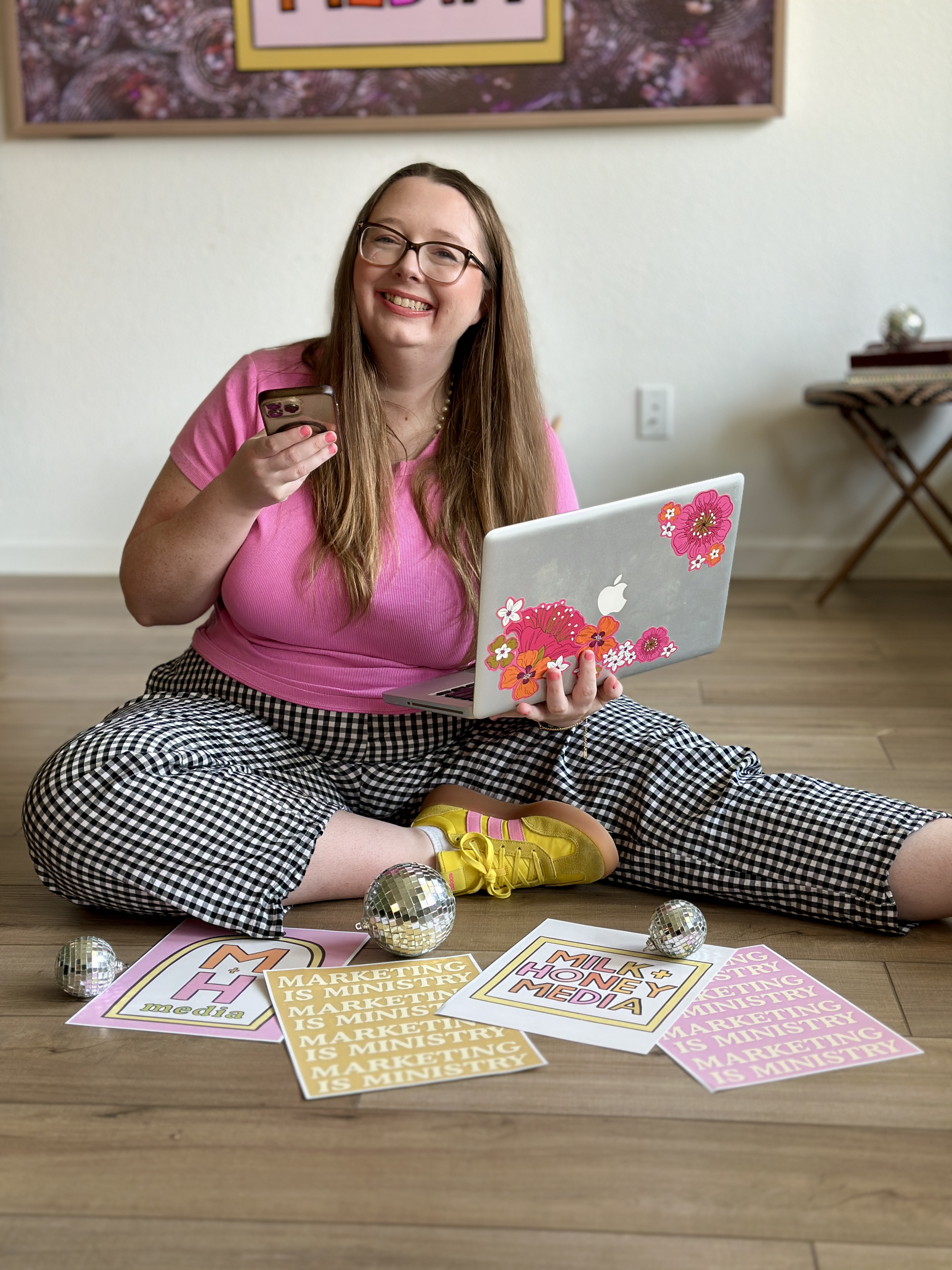Jessie of Milk + Honey Media sitting with her laptop and Marketing is Ministry posters